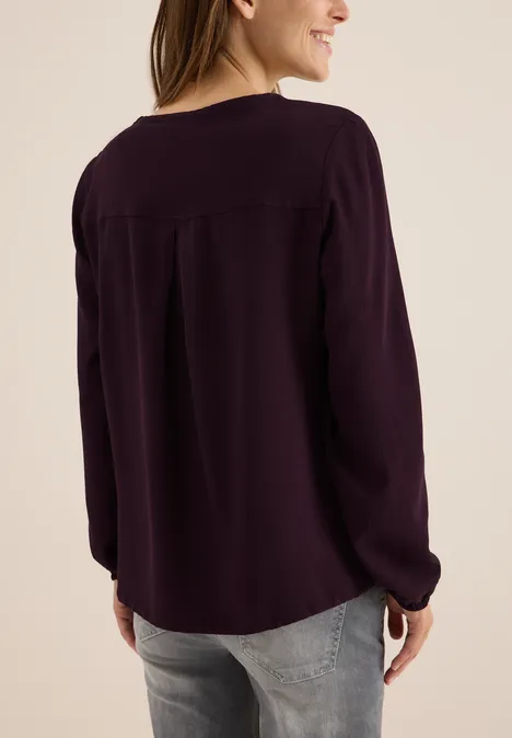 Frau mit lila Langarmbluse und Jeans, von hinten zu sehen.